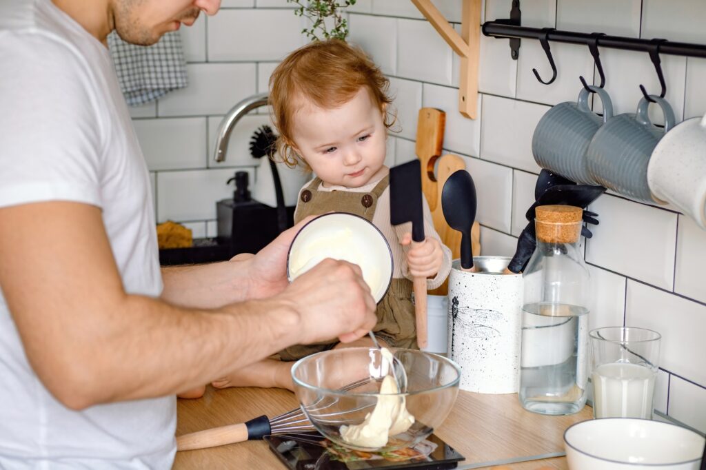A father and baby spending time together cooking. A toddler observing father preparing a meal.