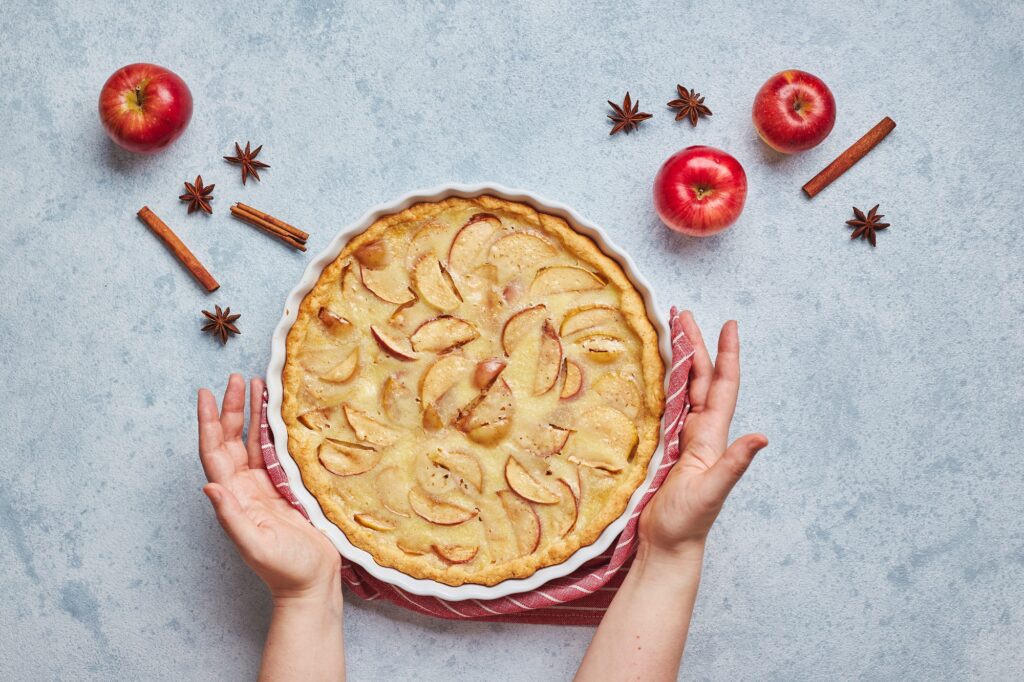 Female hands and homemade apple pie with sour cream filling on light background, top view
