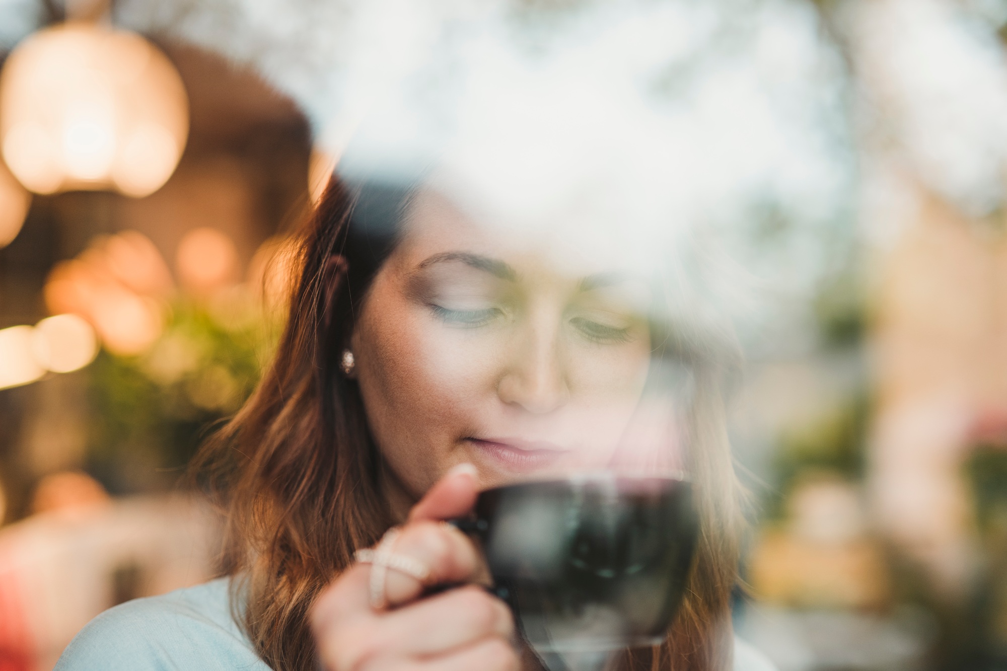 Young woman in a cafe drinking coffee behind windowpane