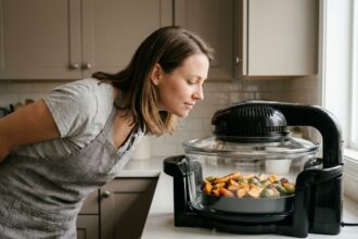 Femme vérifiant la cuisson dans un air fryer noir posé sur un plan de travail de cuisine moderne